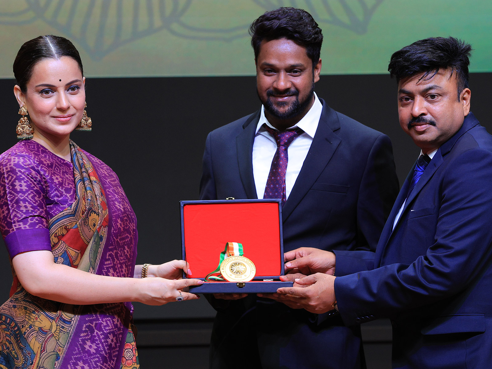On stage at the Rashtriya Ratna Samman 2026, Abu Said Mondal, CMD, and Manas Roy, CEO of Gleestar Jewellery Pvt. Ltd., receive the award for 'India's Most Reliable Jewellery Brand for Purity & Trust' from Ms. Kangana Ranaut