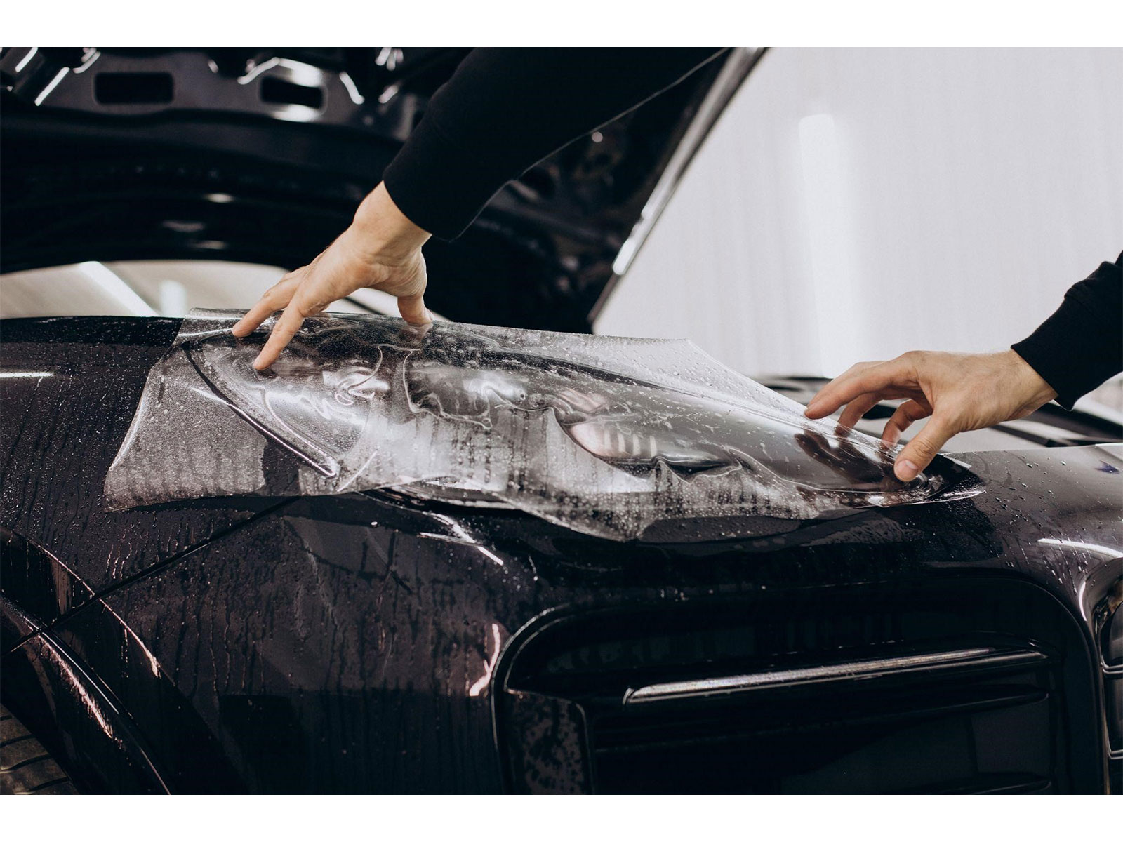 A professional installer applying clear PPF to a luxury car