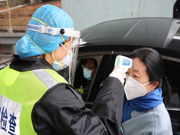 A security officer in a protective mask checks the temperature of a passenger following the outbreak of a new coronavirus in Xianning, China.